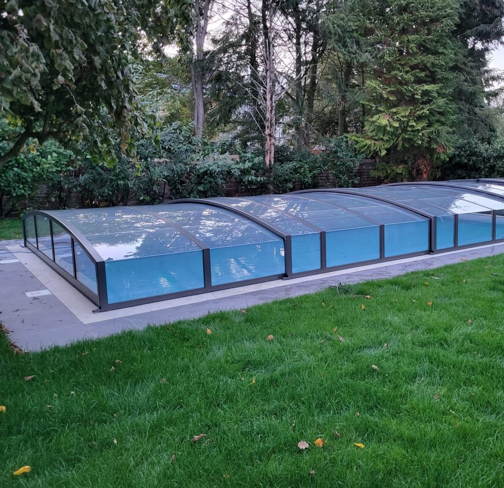 Ein Pool mit einer flachen Glasabdeckung im Garten mit dahinter liegenden Wald